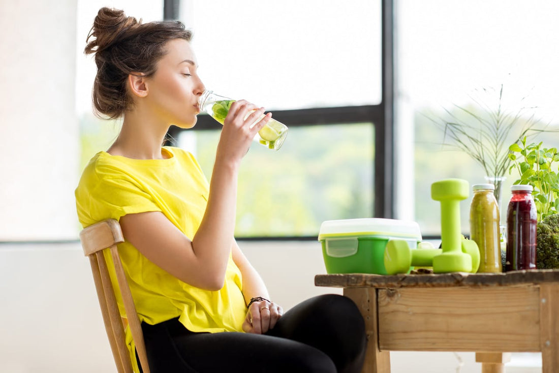 A woman in yellow shirt drinking a glass bottle of water with essential oils in it, detoxifying her body and cells.