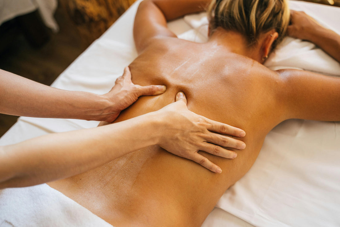 A WELLROSE massage therapist using both hands to massage a woman's bare back using essential oils using the Aromatouch technique to deeply relax her nervous system and reduce stress