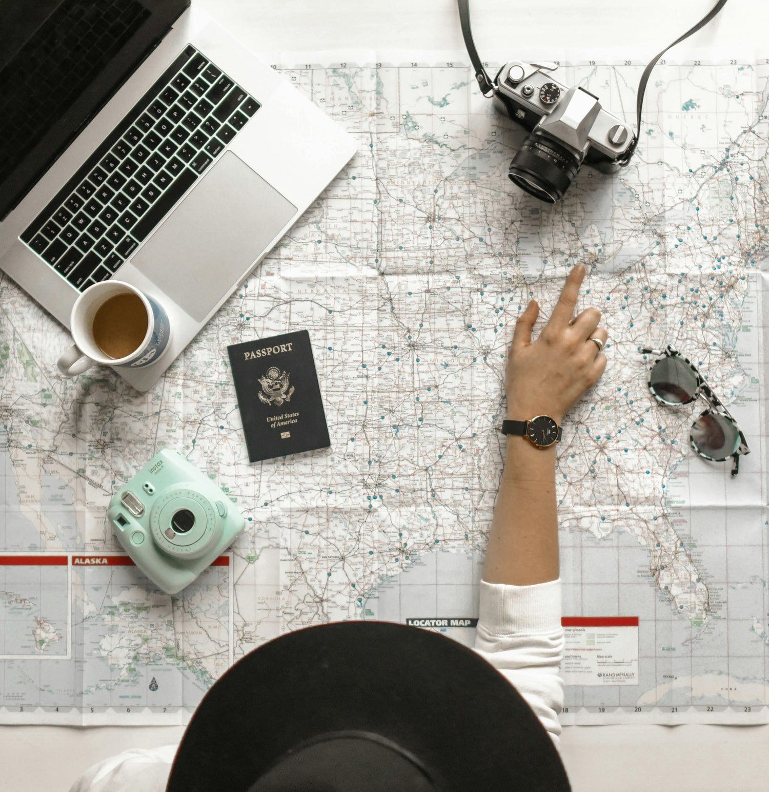 woman pointing on map with laptop passport cameras and sunglasses spread out deciding on where to travel to